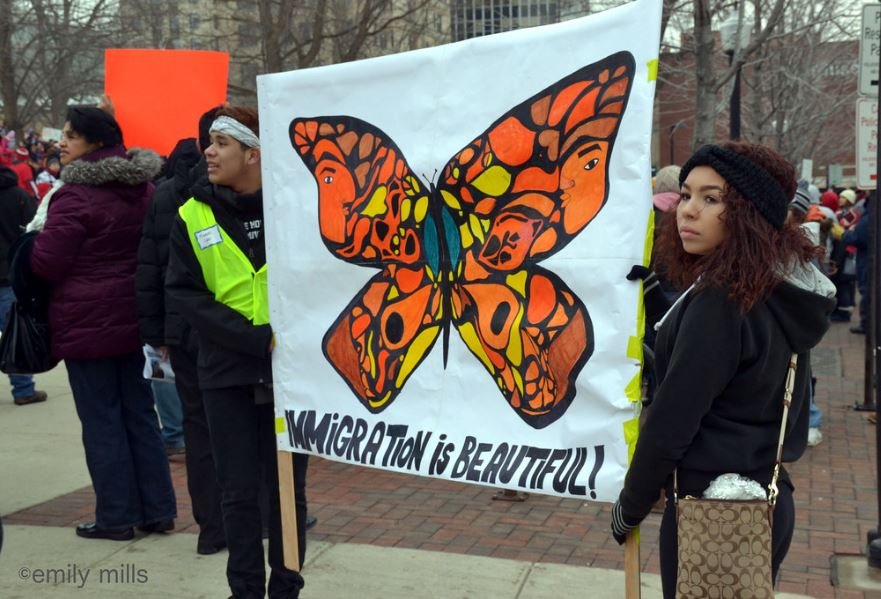 Protect our Immigrants! Photo of protesters with sign with monarch butterfly and "Immigration is Beautiful."