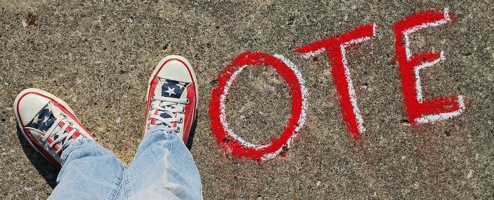 Voter Registration 2020 Kickoff - Photo of "Vote" written on sidewalk with V formed by person standing with red white and blue sneakers.