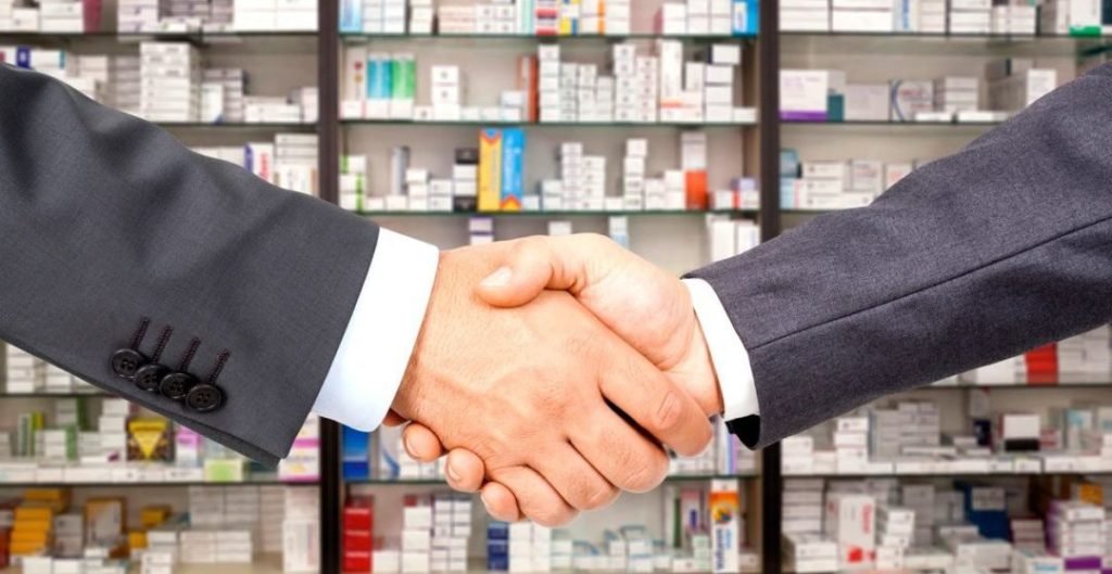 Big Pharma bros in suits shaking hands with medications in the background.