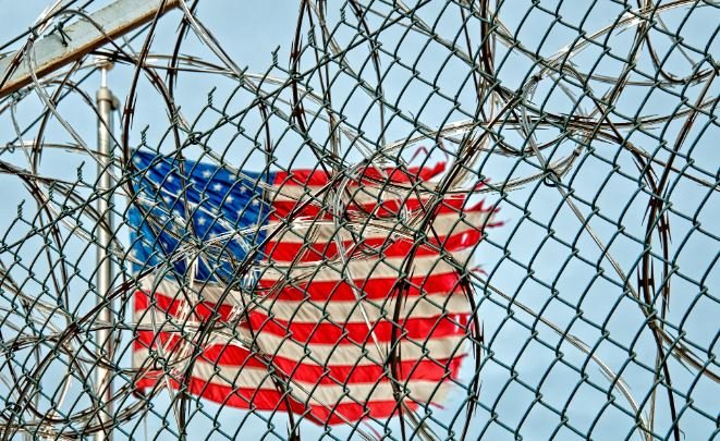 US - American flag behind barbed wire.